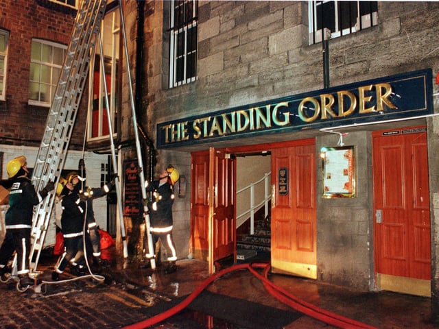 Firefighters erect ladders to tackle flames under the roof of the rear of the Standing Order pub in Rose Street North Lane, 20 February 2000.