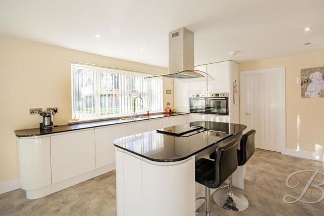 The classy kitchen has underfloor heating, as well as modern, white glass units and two sinks. In the middle is an island, with induction hob and extractor hood.