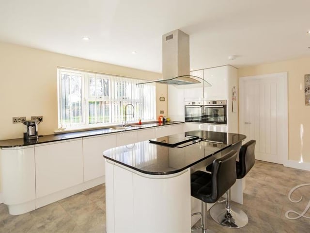 The classy kitchen has underfloor heating, as well as modern, white glass units and two sinks. In the middle is an island, with induction hob and extractor hood.