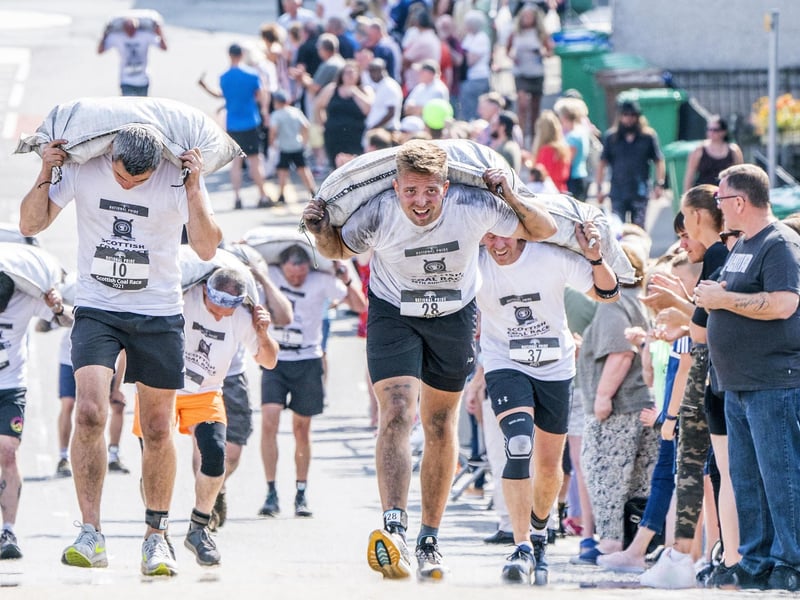 Competitors take part in the Scottish Coal Carrying Championships through the streets of Kelty in Fife. Picture date: Saturday August 28, 2021. PA Photo. The annual event is one of only two Coal Races in the world and the men's race requires participants to carry a 50-kilo bag of coal and the women's race requires a 25-kilo bag of coal to be carried over 1000 metres through the village. Photo credit should read: Jane Barlow/PA Wire
