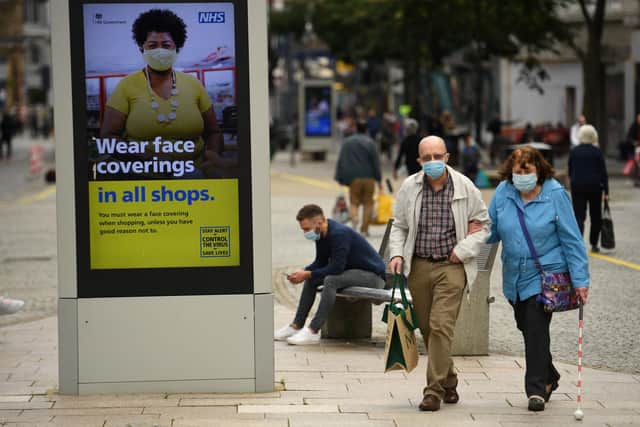 Shoppers wearing face masks walk past a sign calling for the wearing of face coverings in shops, in the city centre of Sheffield (Photo by Oli SCARFF / AFP) (Photo by OLI SCARFF/AFP via Getty Images)