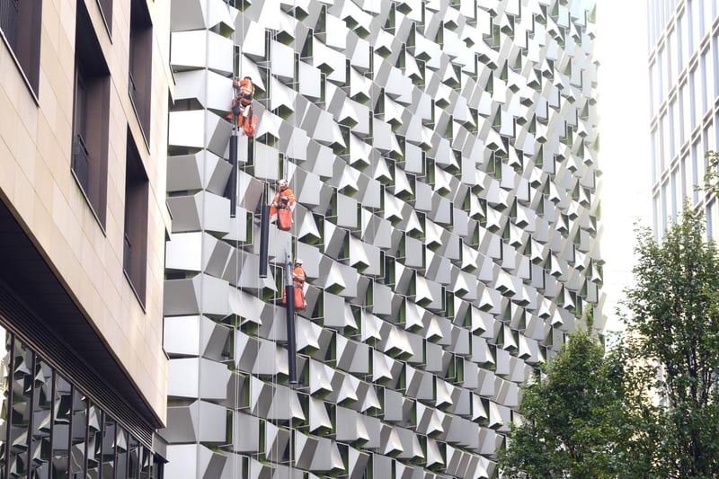 Workers in orange boiler suits line up along facade of the 'Cheese Grater' - Charles Street car park