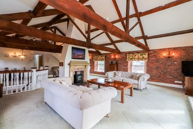 This characterful living space features exposed roof trusses and wooden beams to the vaulted ceiling, part exposed brick walls and a central fireplace which is set in a stone surround.