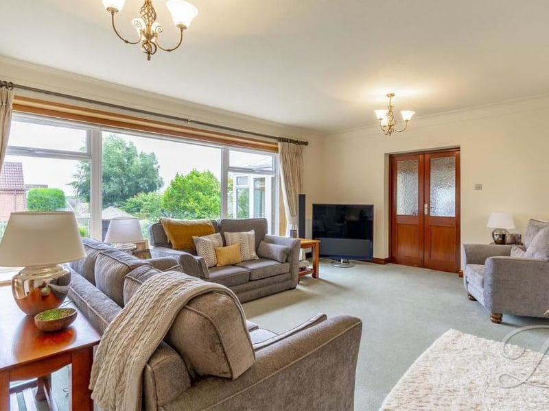 Another view of the bright and airy living room, which has windows to the front and back. Carpeted, it has three central-heating radiators.