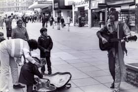 Pictured in action in Fargate complete with cap, bells and guitar, is busking jester, Roger Pugh. In the background you can see the long gone Wimpy Bar, Peter Lord's shoe shop, and Ratner's jewellers, October 1983