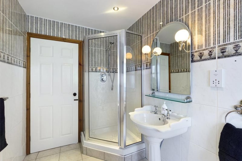 Family bathroom with modern white suite comprising low level WC, pedestal wash basin, bath and tiled shower enclosure with mixer shower; wall and floor tiling, feature mirror with wall lights, inset spot lighting, radiator panel and sealed unit double glazed window to the rear elevation.