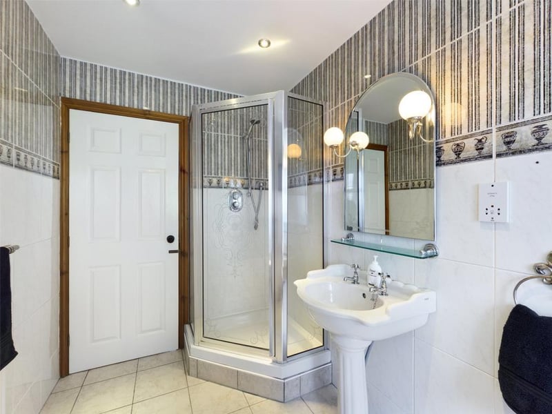 Family bathroom with modern white suite comprising low level WC, pedestal wash basin, bath and tiled shower enclosure with mixer shower; wall and floor tiling, feature mirror with wall lights, inset spot lighting, radiator panel and sealed unit double glazed window to the rear elevation.