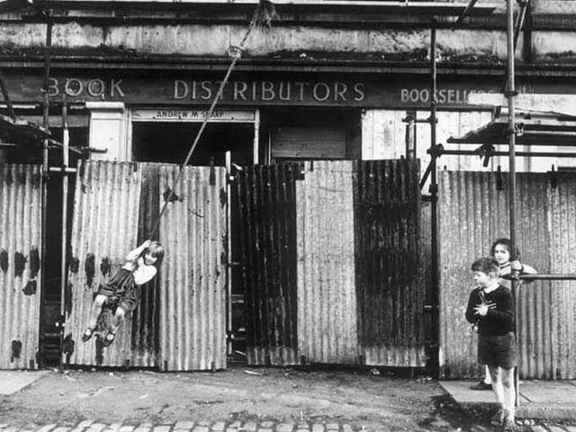 Children play with a rope swing on the scaffolding at India Place, where buildings were being knocked down, 1960s.