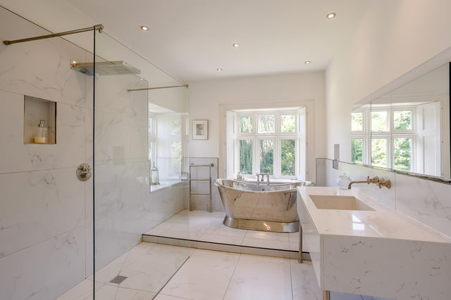 The bathroom is impressive with its white marble tiled floor and walls and polished nickel fittings. There is a stylish open-ended shower and to the far end of the room a raised section showcasing a polished nickel stand alone bath.