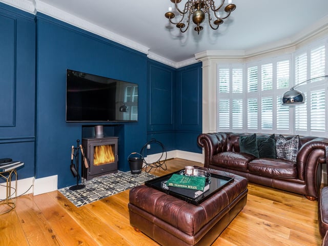 A "charming reception" room with a bay window to the South elevation with wooden shutters, multi-fuel stove set on tiled hearth, feature arched recess and decorative cornice to ceiling.