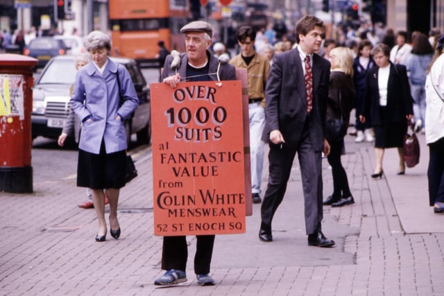 An elderly man wearing a sandwich board advertising suits from Colin White Menswear walks through the city centre Glasgow, August 1990