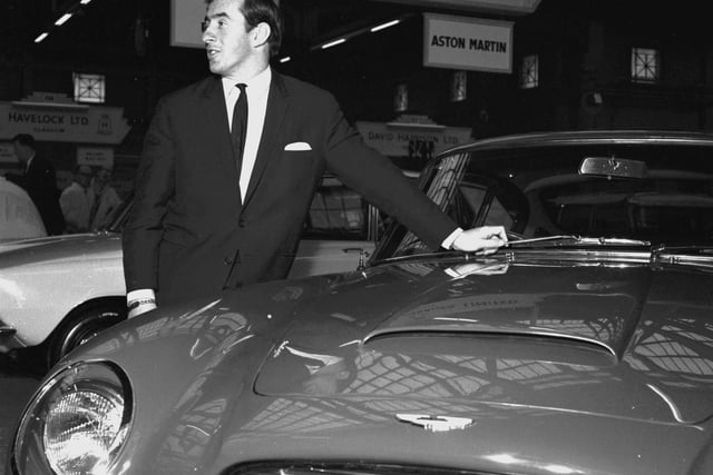 Racing driver Jackie Stewart stands beside an Aston Martin DB6 at the Scottish Motor Show in the Kelvin Hall, Glasgow, November 1965