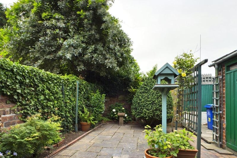 Rear garden - Wall enclosed with timber access gate opening onto the rear service path; paved with raised flower beds and a variety of mature plants, flowers and shrubs, tool store and garden taps.