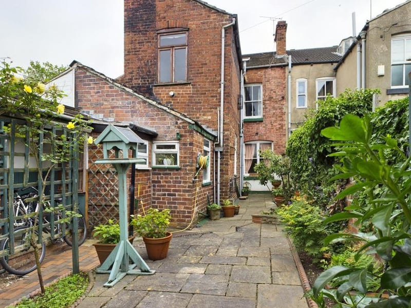 Rear garden - Wall enclosed with timber access gate opening onto the rear service path; paved with raised flower beds and a variety of mature plants, flowers and shrubs, tool store and garden taps.