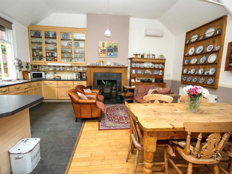Multi-fuel burner on a tiled hearth with a wooden surround, wall-mounted air conditioning unit, wall-mounted original display cupboard, oak timber and tiled flooring and two windows to the front elevation.