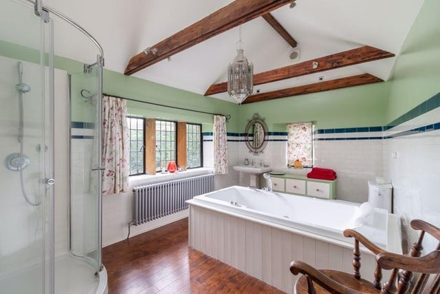 There are three bathrooms in total, including this country-style suite with wooden floors, oak beams overhead, central bathtub and standing corner shower.