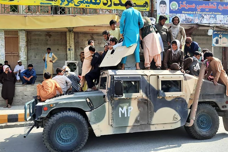 Taliban fighters and local residents sit on an Afghan National Army (ANA) Humvee vehicle along the roadside in Laghman province