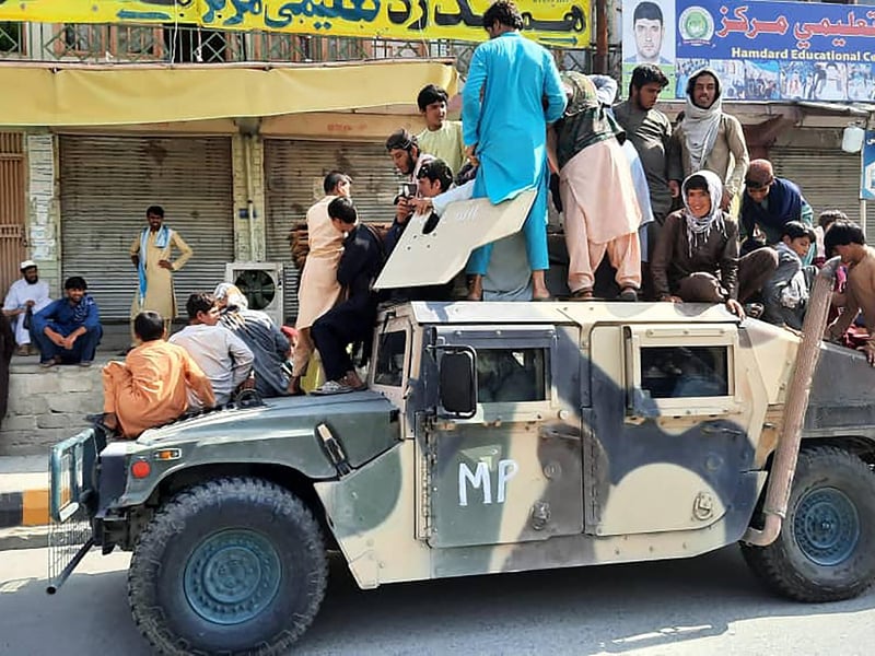 Taliban fighters and local residents sit on an Afghan National Army (ANA) Humvee vehicle along the roadside in Laghman province