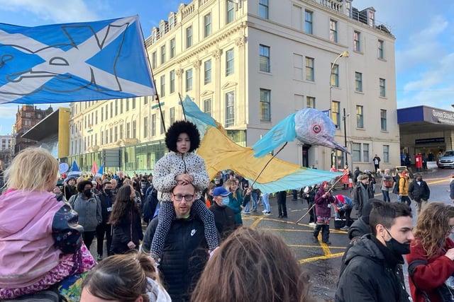 A child activist on the shoulders of an adult as crowds march. A "Yes" for Scottish independence flag is blowing behind them.