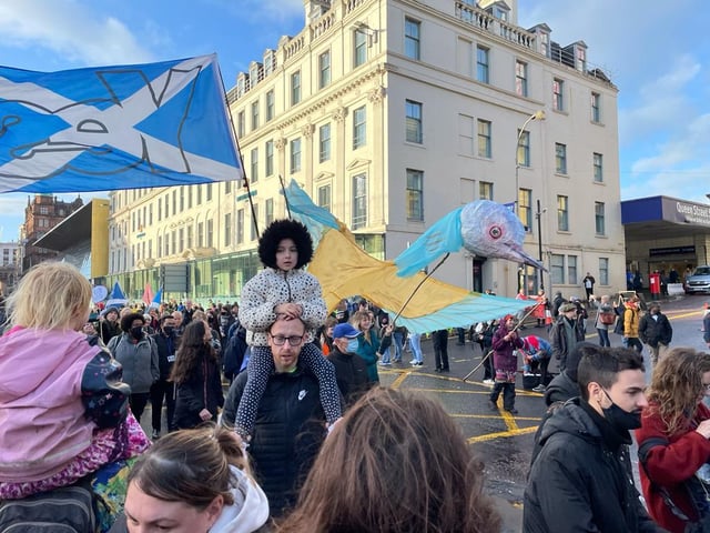 A child activist on the shoulders of an adult as crowds march. A "Yes" for Scottish independence flag is blowing behind them.