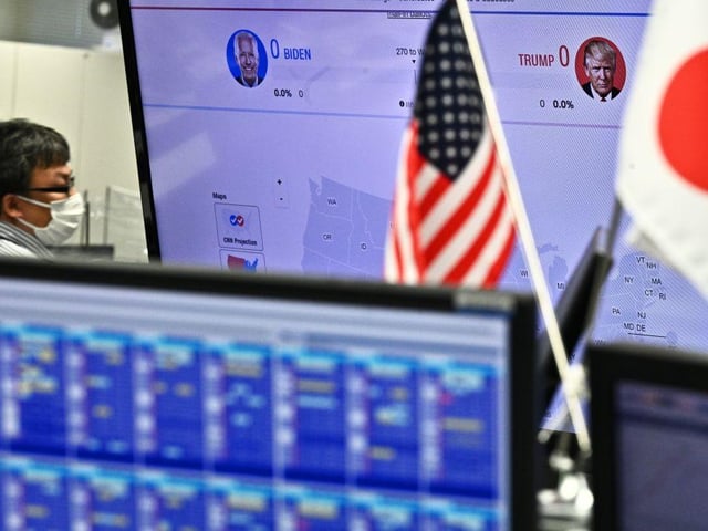 An Employee of a foreign exchange trading company observes the US presidential elections as a news channel shows portraits of candidates Donald Trump (R) and Joe Biden, in Tokyo on November 4, 2020.