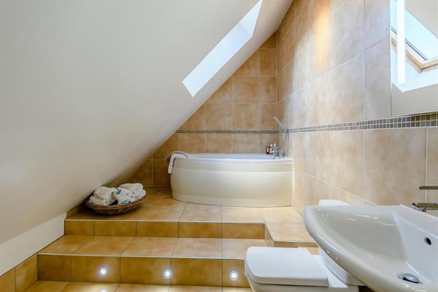 This en suite bathroom boasts a modern three-piece suite that includes a panelled bath with mixer tap and shower over. There is also a pedestal wash hand basin, low-flush WC, chrome, heated towel-rail and a Velux roof window.