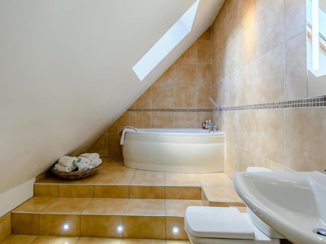 This en suite bathroom boasts a modern three-piece suite that includes a panelled bath with mixer tap and shower over. There is also a pedestal wash hand basin, low-flush WC, chrome, heated towel-rail and a Velux roof window.