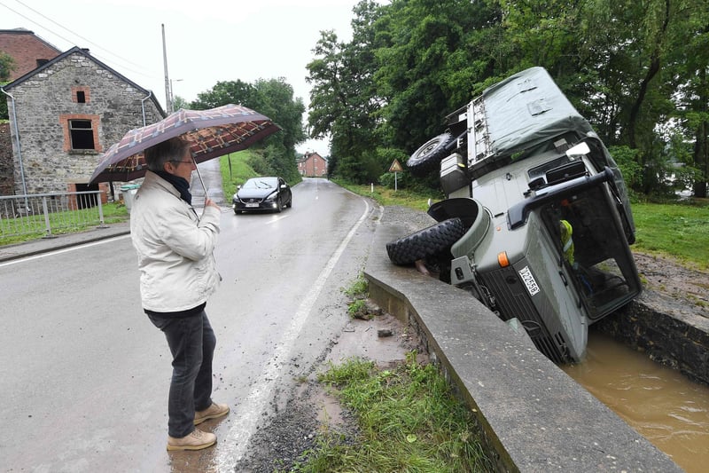 A woman stands under an umbrella as she looks at an  Belgian army vehicle overturned in a ditch of water near the town of Rochefort on July 16, 2021. - The death toll from devastating floods in Europe soared to at least 108 on July 16, 2021