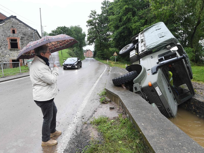 A woman stands under an umbrella as she looks at an  Belgian army vehicle overturned in a ditch of water near the town of Rochefort on July 16, 2021. - The death toll from devastating floods in Europe soared to at least 108 on July 16, 2021