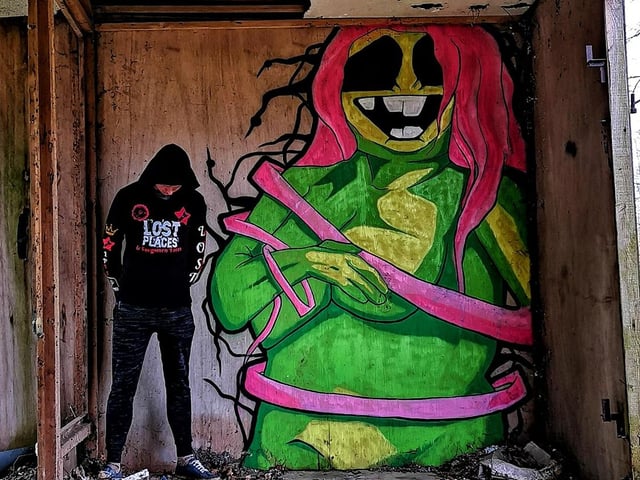 Urban explorer Lost Places & Forgotten Faces next to a piece of art by Brayk.
