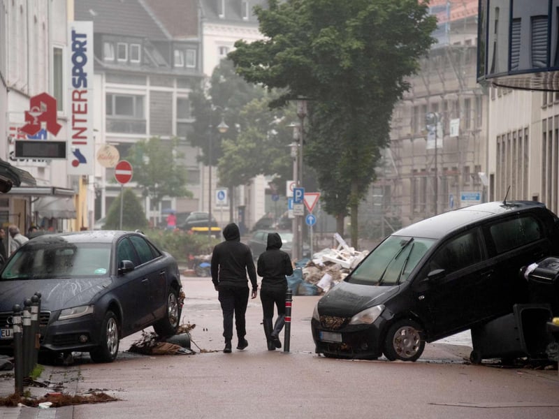 People pass by destroyed cars after the floods caused major damage in Euskirchen, western Germany, on July 16, 2021. - The death toll from devastating floods in Europe soared to at least 93, most of them in western Germany, where emergency responders were searching for hundreds of missing people. (Photo by SEBASTIEN BOZON / AFP)