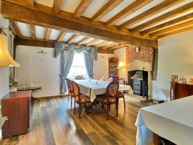 The dining room includes a feature stone and brick fireplace with stove. The ceiling is heavily beamed, and there are inset timber frames to the walls.