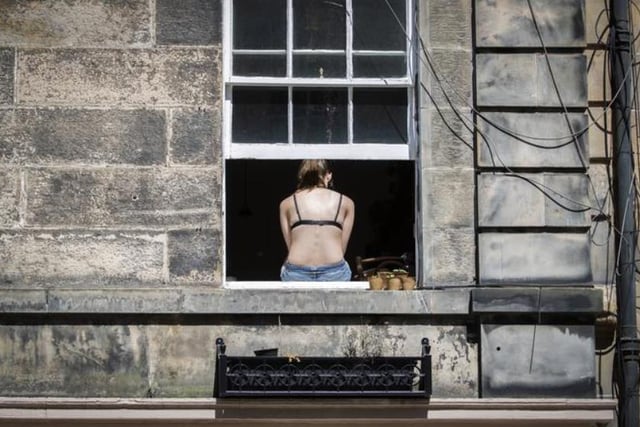 A woman sunbathes in the good weather at the window of her tenement flat in Edinburgh. Photo: Jane Barlow/PA Wire