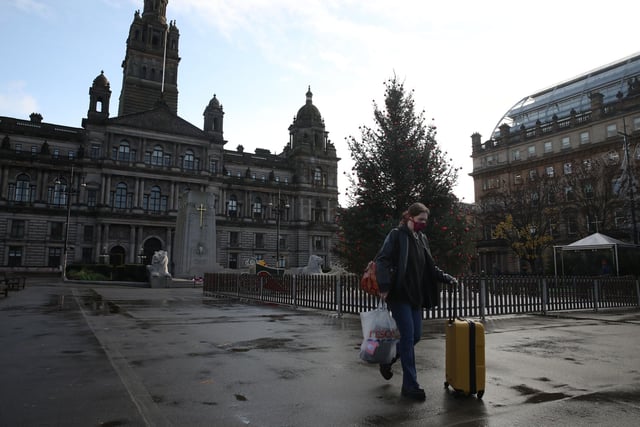 A woman pushes her suitcase through a quiet George Square in Glasgow.