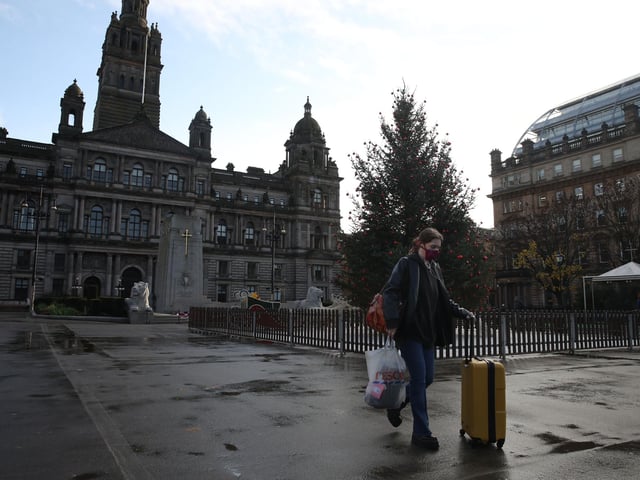 A woman pushes her suitcase through a quiet George Square in Glasgow.