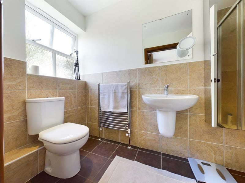 Ensuite shower room with white suite comprising low level WC, wall mounted wash basin and tiled shower enclosure with mixer shower.