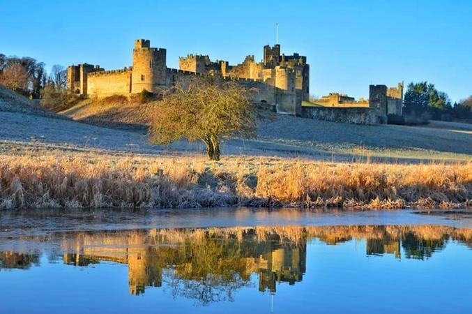 Alnwick Castle with its reflection in the River Aln.