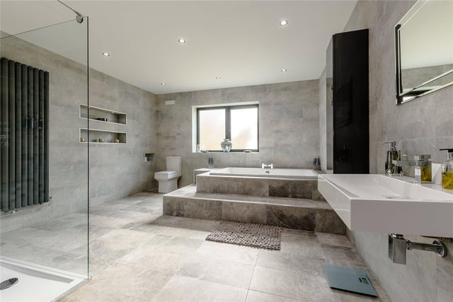 The large family bathroom benefits from a walk-in shower, huge bath, toilet and sink, and modern marble-effect tiling.