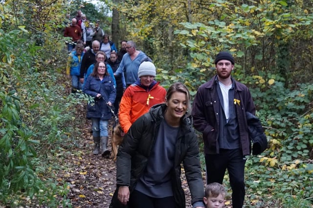 Supporters of all ages wander through a wooded area of the site
