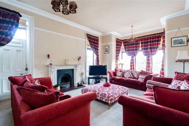 The well-presented living room features a stone mullion bay window offering stunning views over the sprawling grounds, with a wealth of seating space and a fireplace at its heart.
