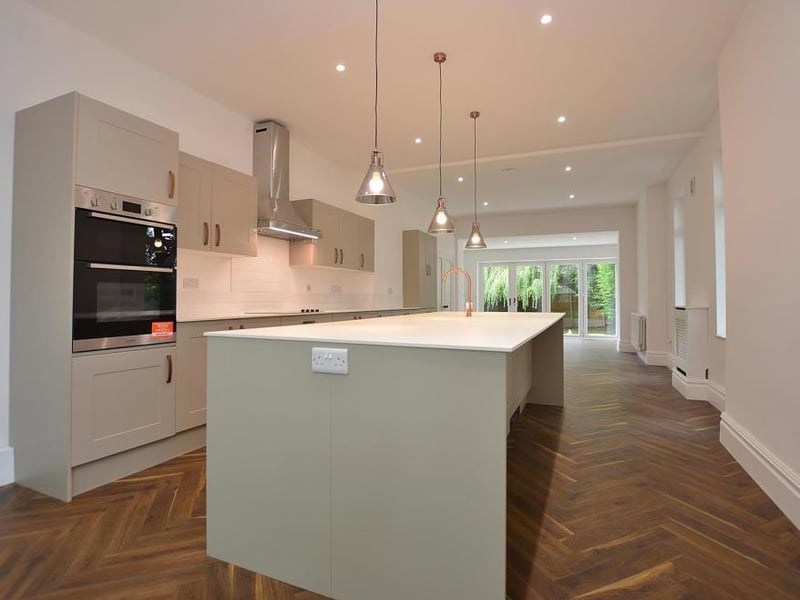 The kitchen features a tasteful range of modern, yet timeless, cupboards, base units and drawers in a beautiful, neutral colour. There are also sleek working surfaces, a large central island, sink and four-ring hob with wall-mounted extractor hood.