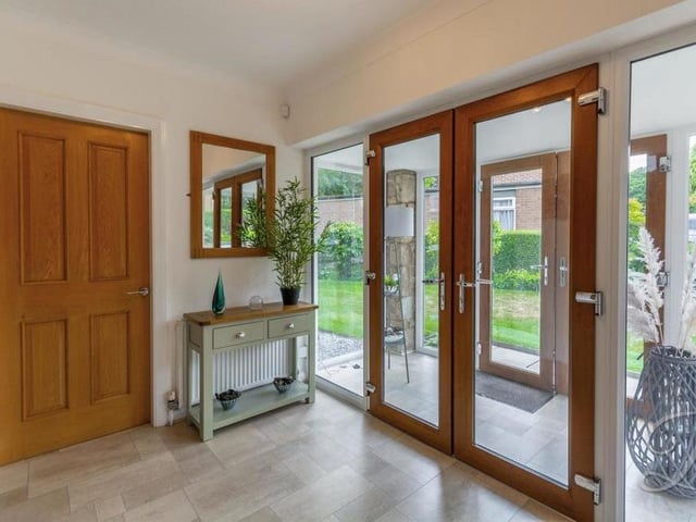 A spacious entrance hallway with double doors, a central-heating radiator and a cupboard for storage. A carpeted staircase leads to the first floor.
