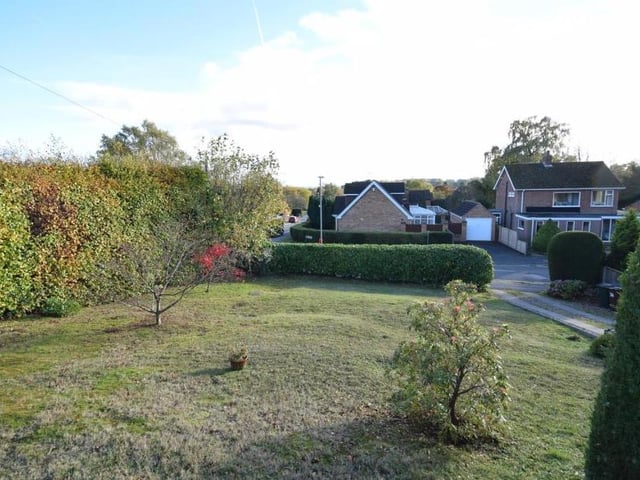 A view from the front of the bungalow, showing its elevated position and long, lawned garden. The lawn is screened by established hedges, while a lengthy driveway offers ample parking space and leads to an integral garage that has power, lighting and a useful tap.
