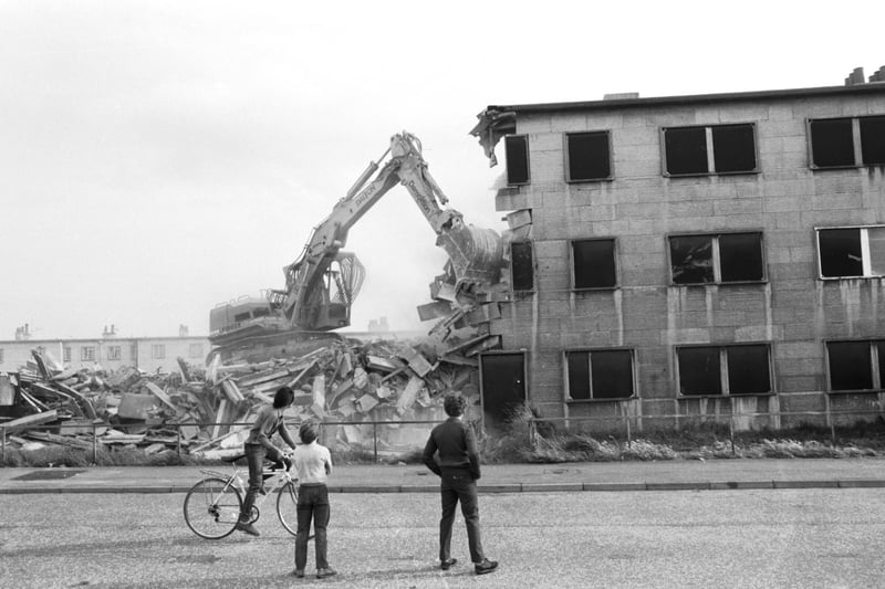Three boys watch as a bulldozer demolishes the firts of the Orlit (pre-cast concrete, 'prefabs') houses at Bingham Broadway in Edinburgh, September 1985.