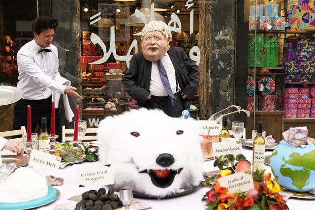 An actor dressed in a mask depicting Prime Minister Boris Johnson, dines at a banquet of environmental and climate degradation during a performance on Buchanan Street, during the Cop26 summit in Glasgow.