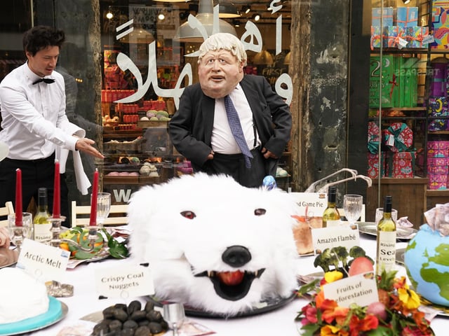 An actor dressed in a mask depicting Prime Minister Boris Johnson, dines at a banquet of environmental and climate degradation during a performance on Buchanan Street, during the Cop26 summit in Glasgow.
