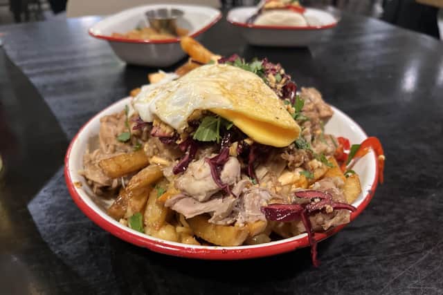 The Full Works, features glazed sticky chicken on skin-on fries, topped with sweet soy, chilli mayo, garlic sriracha, pickled asian slaw, melted cheese in layers and a crispy orange runny egg on top.