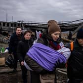 A woman carrying her baby crosses a destroyed bridge as they flee the city of Irpin in Ukraine