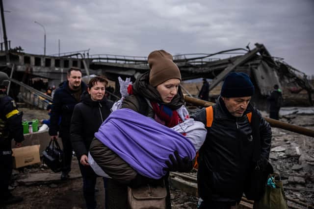A woman carrying her baby crosses a destroyed bridge as they flee the city of Irpin in Ukraine