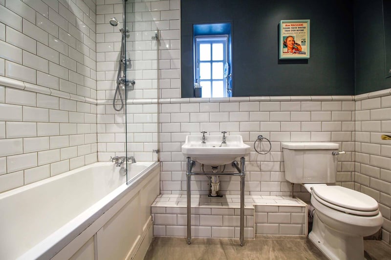 With a three-piece white suite comprising of a panelled bath with mixer shower over and glass shower screen, low flush WC, mounted wash hand basin. Part tiled high gloss white tiling to the walls. Porcelain Dove tiling to the floor. Downlighting.